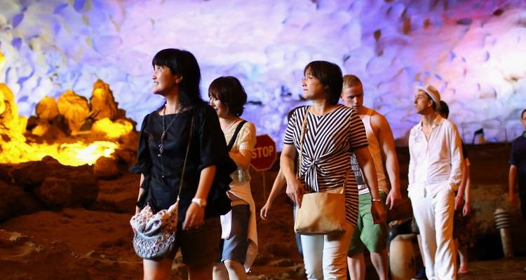 Group of tourists exploring a colorful, illuminated cave.