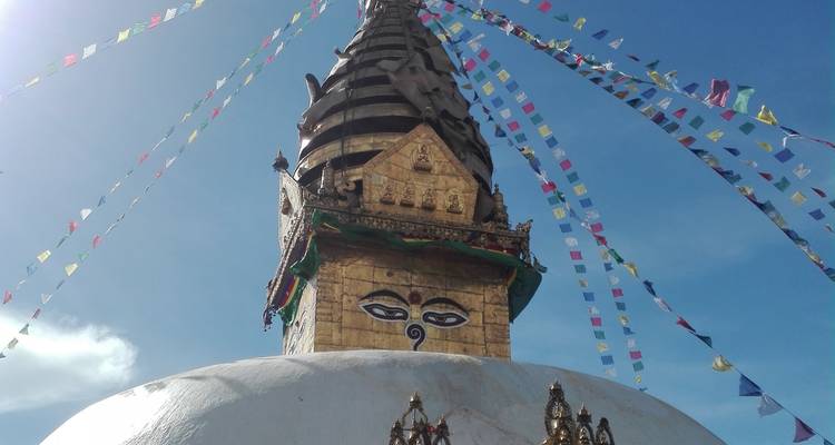 Eine Stupa mit Gebetsfahnen vor einem klaren blauen Himmel.