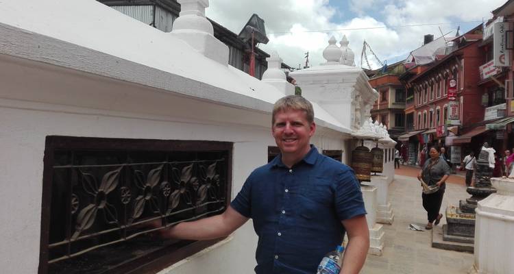 Ein Mann, der neben einem weißen Denkmal in einer Stadtstraße posiert.