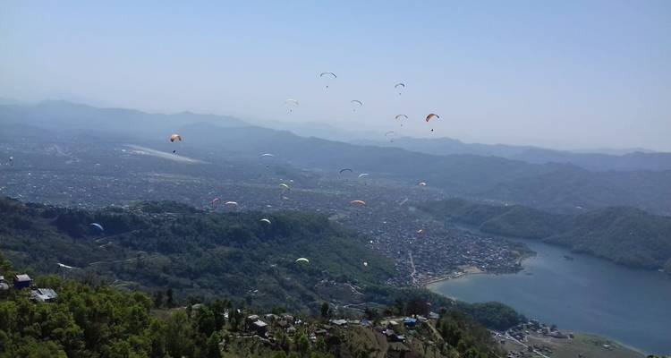 Zicht op een stad en meer met talrijke paragliders in de lucht.