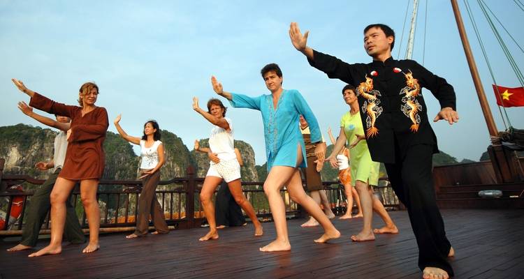 Mensen die tai chi beoefenen op een bootdek met een zonsopgang op de achtergrond.