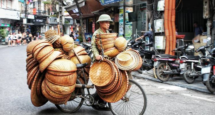 Man cycling with multiple baskets through a street.