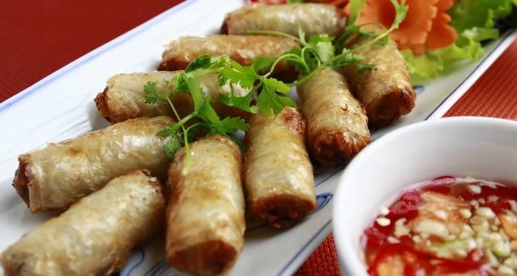 Plate of spring rolls served with dipping sauce and garnish.