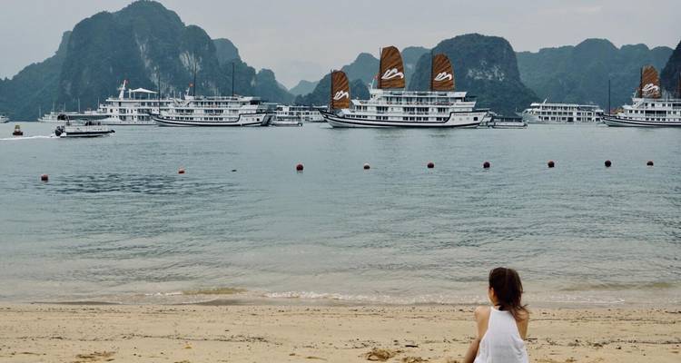 Frau, die an einem Strand sitzt mit Kreuzfahrtschiffen in der Halong-Bucht.