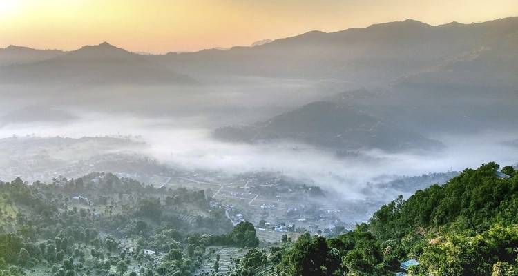 Fog-filled valley with rising sun and surrounding hills.