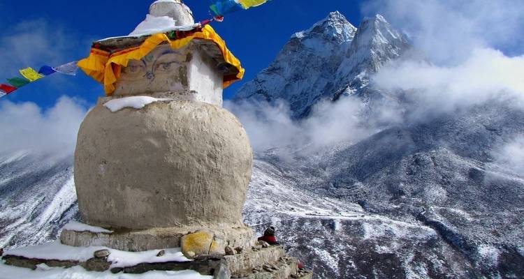 Stupa with prayer flags against a backdrop of snowy mountains.