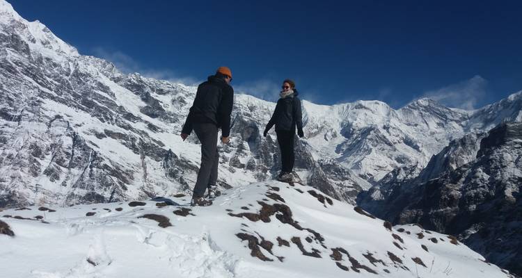Deux personnes sur une montagne enneigée avec des sommets au loin.