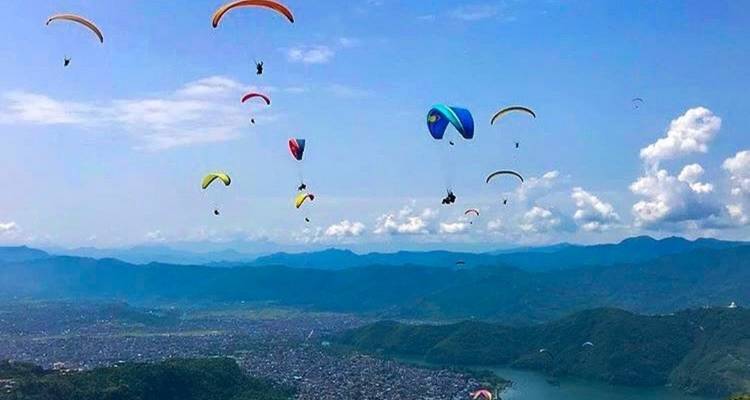 Des parapentistes planant au-dessus d'une ville avec des collines en arrière-plan.