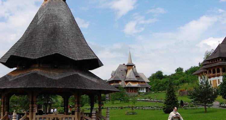 Traditionelle Holzbauten in einer grünen Landschaft mit einer Person in traditioneller Kleidung.