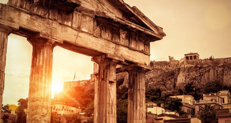 Ancient columns of the Roman Agora lit by warm sunset rays with the Acropolis hill behind