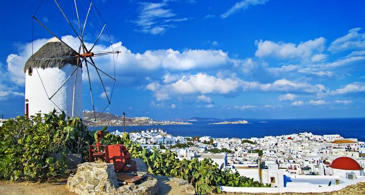 Whitewashed windmill in foreground with panoramic view over Mykonos town and deep-blue Aegean Sea