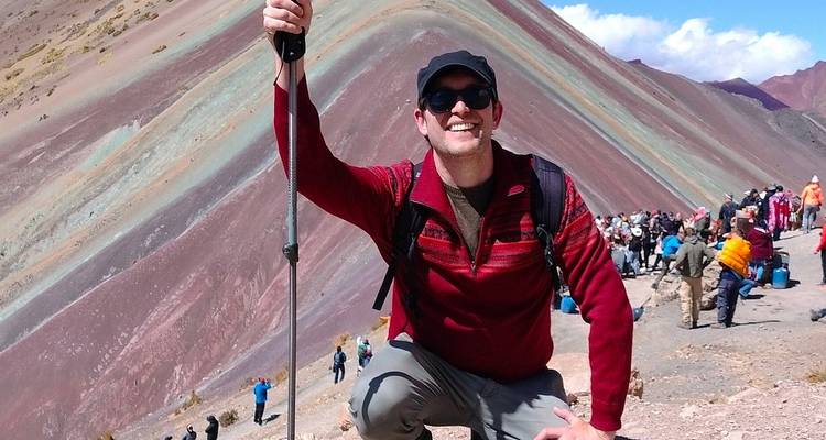 Una persona sonriendo y arrodillada con un bastón de trekking en la Montaña Arcoíris.