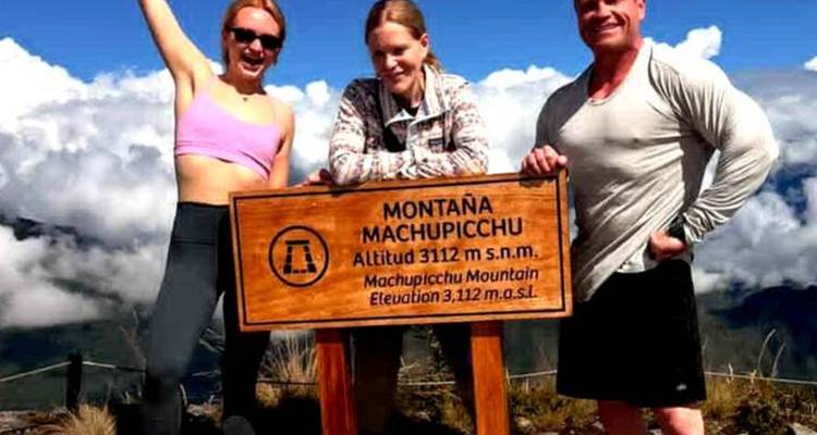 Grupo celebrando en la cumbre de la montaña Machu Picchu junto a un cartel de altitud.