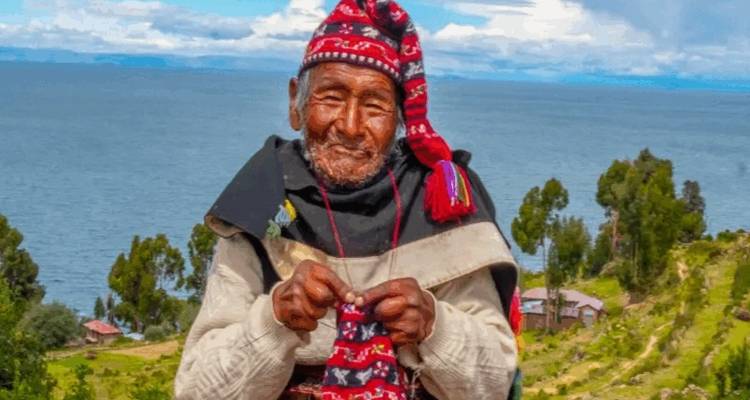 Homme âgé en vêtements traditionnels péruviens avec un lac et des champs en arrière-plan.