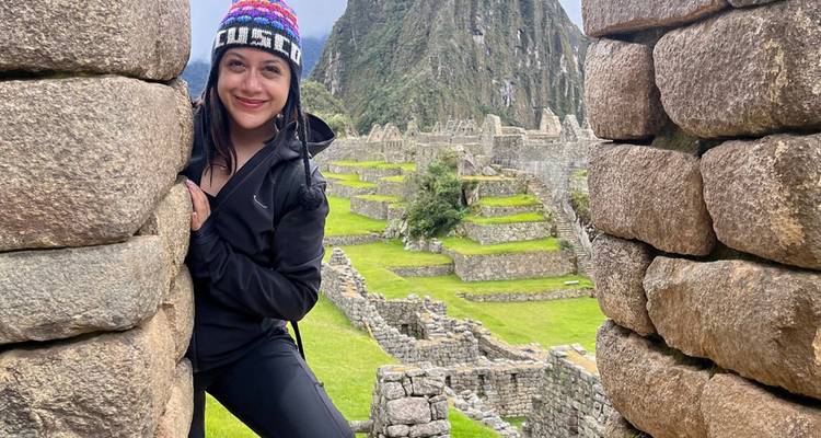 Femme posant près d'une structure en pierre avec le Machu Picchu en arrière-plan.