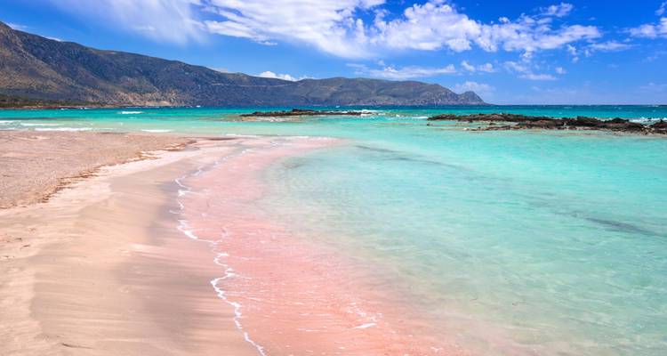 Mar turquesa y playa arenosa con montañas al fondo.