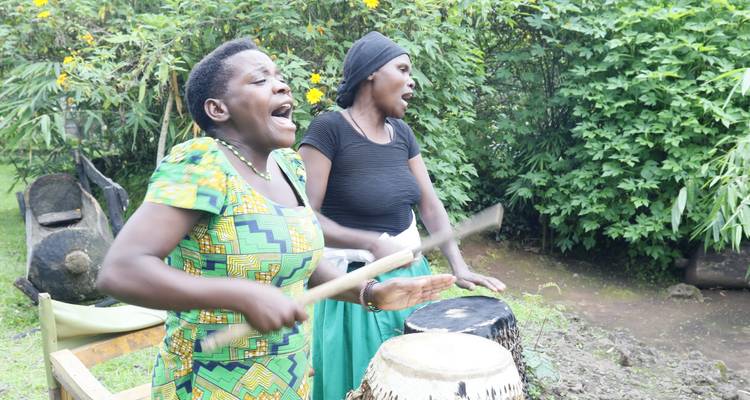 Zwei Frauen, die in einer Umgebung im Freien trommeln und singen.