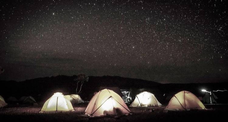 A starry night sky over a camping site with lighted tents.