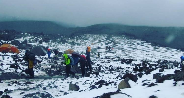 Excursionistas en un paisaje rocoso cubierto de nieve con tiendas de campaña.