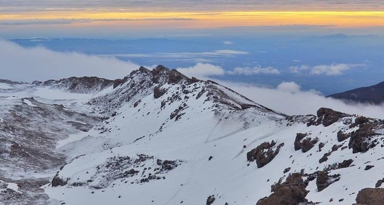 Snow-covered mountain ridges at dawn with clouds below.