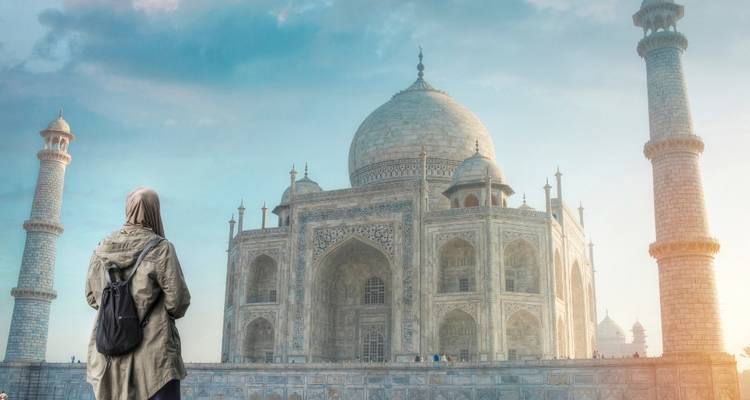 Das Taj Mahal mit einem Besucher, der es betrachtet, unter einem klaren Morgenhimmel.