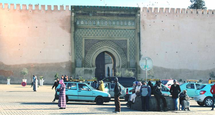 Eine Gruppe von Menschen vor einem kunstvoll gestalteten Tor mit Autos drumherum.