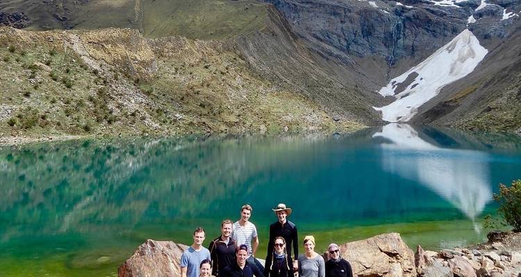 Group of people posing by a scenic lake with mountain backdrop.
