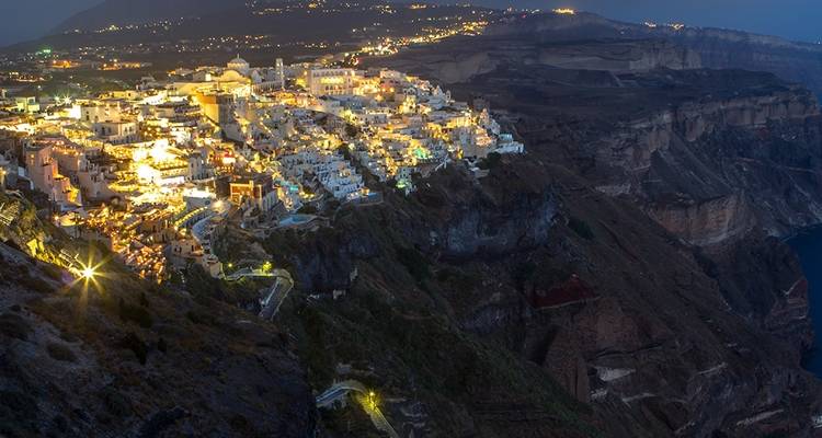 Night view of Santorini with illuminated buildings on a cliffside.