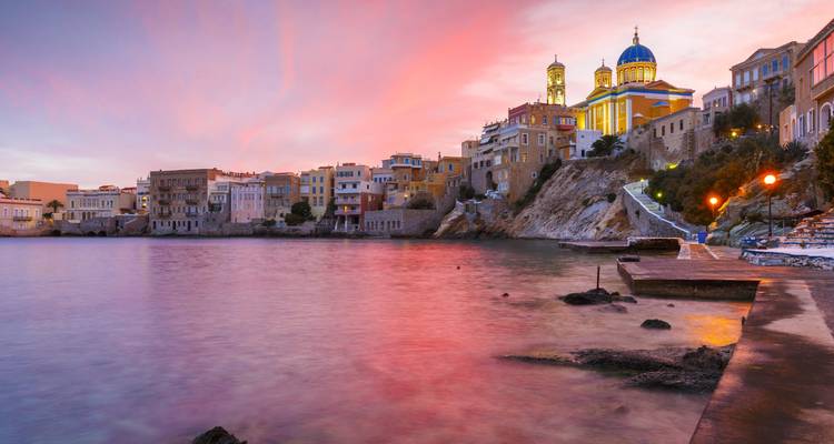 Vue du coucher de soleil sur le quartier de Vaporia à Syros avec une église sur une colline.