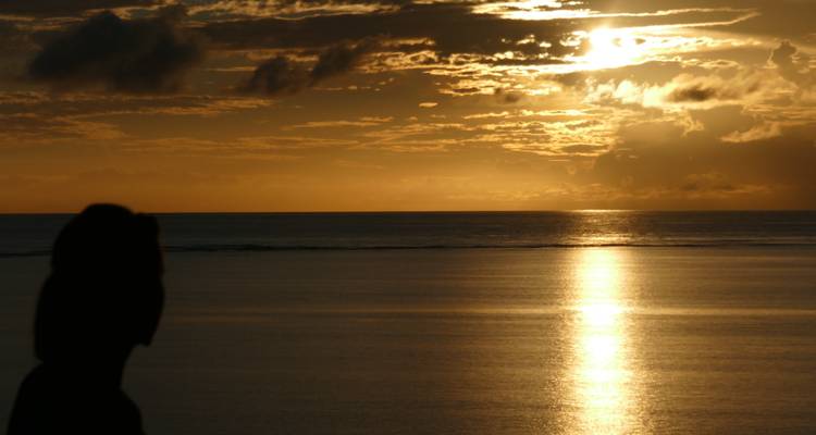 Silhouette of a person against a dramatic sunset over the ocean.