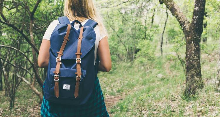 Mujer con una mochila caminando por un sendero boscoso.