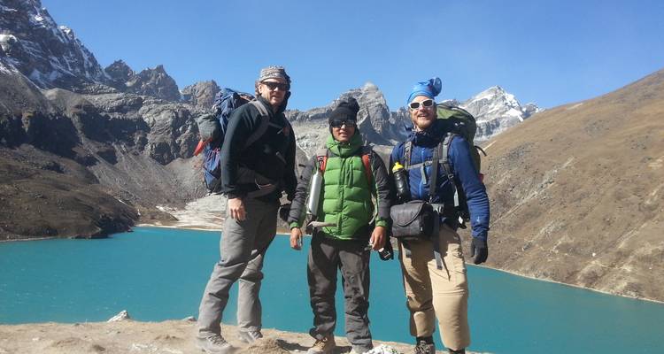 Group of trekkers posing with a lake and mountains in the background.