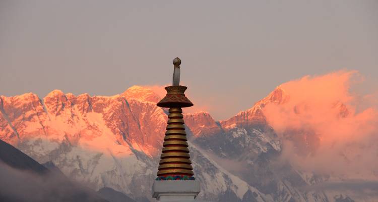 Mountain peaks illuminated by the setting sun, with a stupa in the foreground.