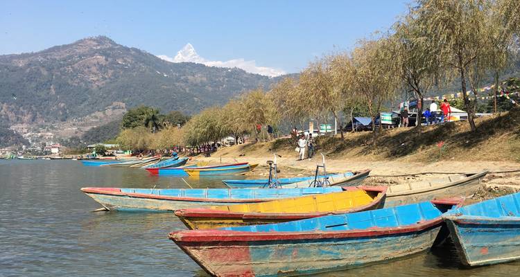Bunte Boote aufgereiht an einem Seeufer mit fernen Bergen.