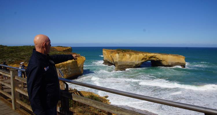 Un visiteur montre du doigt l'arche de la mer du London Bridge le long de la Great Ocean Road en Australie par une journée ensoleillée.