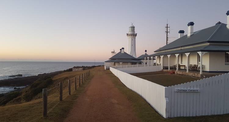 Leuchtturm mit Häuschen am Meer am Abend.