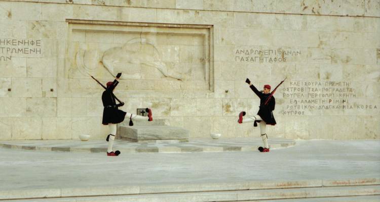 Guards performing a ceremonial march in front of a stone wall.