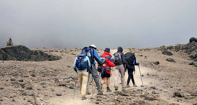 Un grupo de excursionistas caminando por un sendero rocoso en condiciones de niebla.