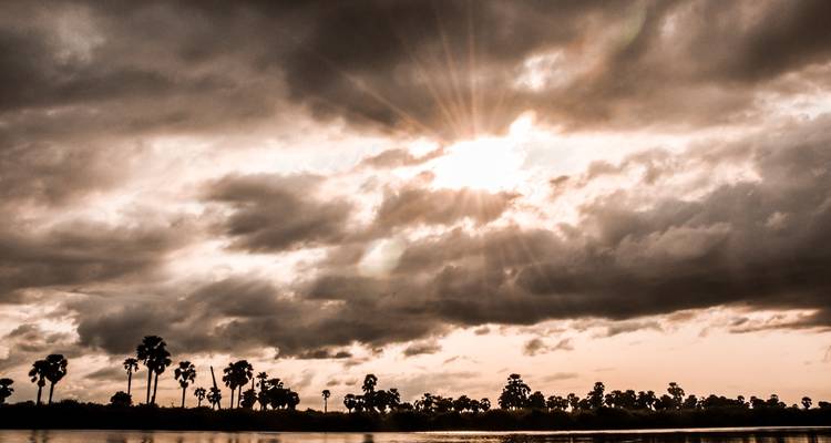 Bewolkte lucht met zonnestralen boven een landschap.