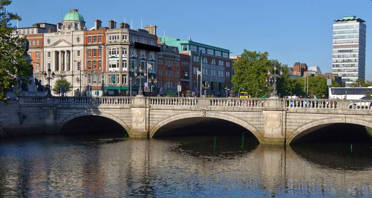 Puente de piedra que atraviesa un río tranquilo con edificios históricos y modernos alineados en los muelles de Dublín.