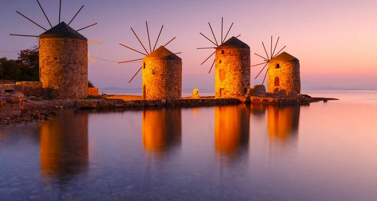 Los molinos de piedra históricos se reflejan en aguas tranquilas durante un amanecer en tonos pastel.