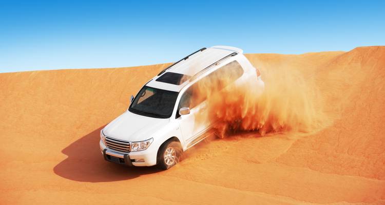 A white SUV driving through sand dunes in a desert.