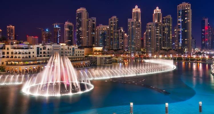 Illuminated city skyline with a fountain show at night.