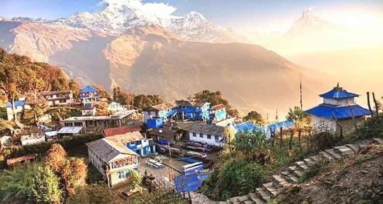 Een dorp gelegen op een bergflank met blauwe daken en besneeuwde toppen in de verte.