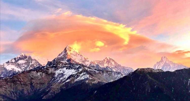 Zonsondergangzicht over een bergketen met levendige wolken en besneeuwde toppen.