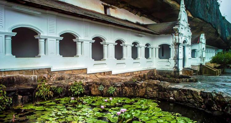 Un monasterio con columnas de piedra y un estanque de lotos en un entorno sereno.