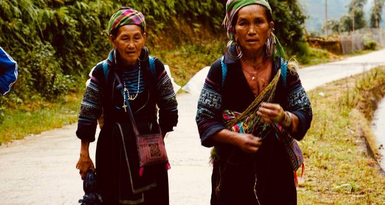 Zwei einheimische Frauen in traditioneller Kleidung gehen auf einem unbefestigten Weg.