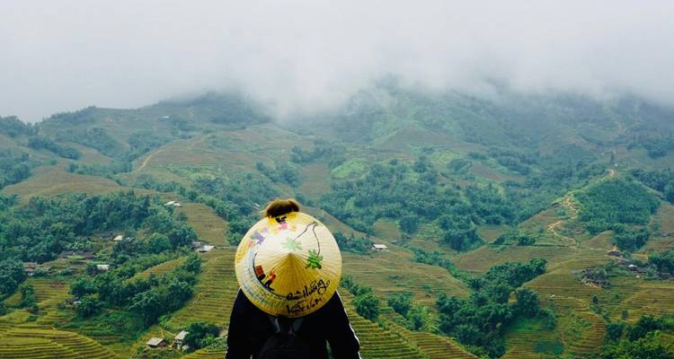 Person mit einem konischen Hut, die terrassierte Felder überblickt.