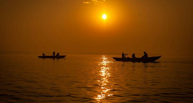 Silhouetted rowboats gliding on calm river at golden sunrise with glowing reflection