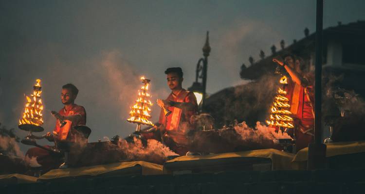 Priests performing evening aarti with flaming lamps and rising incense smoke